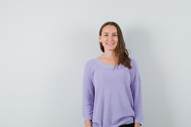 Mujer joven sonriendo en blusa lila y mirando alegre. vista frontal. espacio para texto