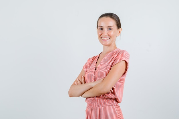 Mujer joven sonriendo con los brazos cruzados en traje de rayas, vista frontal.