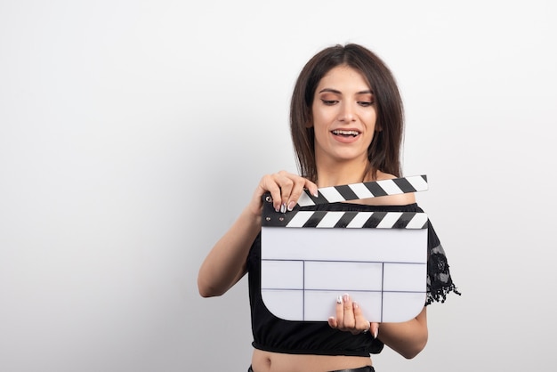 Mujer joven sonriendo con una claqueta de cine.