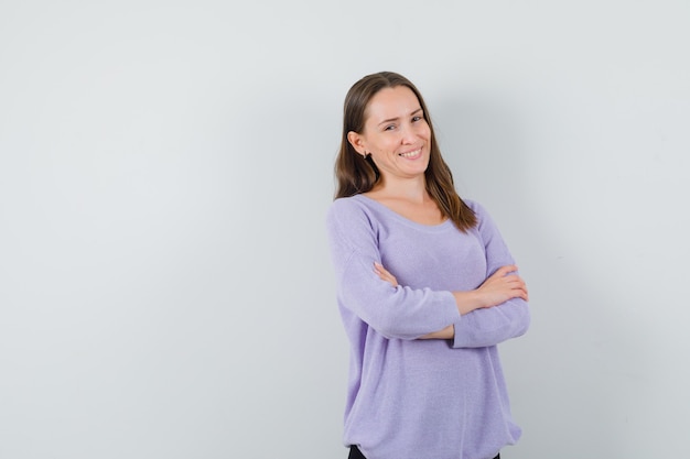 Mujer joven sonriendo mientras mantiene los brazos cruzados en blusa lila y luciendo positiva. vista frontal. espacio para texto