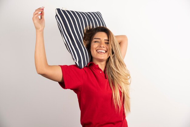 Mujer joven sonriente abrazando una almohada sobre fondo blanco.