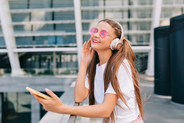 Mujer joven sonriente y bailando sosteniendo un teléfono inteligente y escuchando música en auriculares