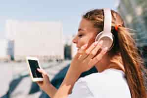 Foto gratuita mujer joven sonriente y bailando sosteniendo un teléfono inteligente y escuchando música en auriculares
