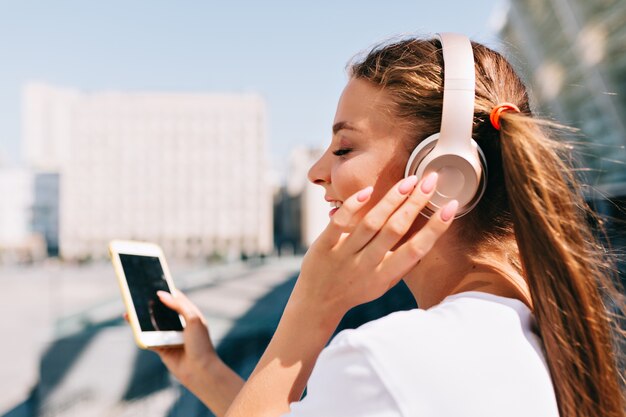 Mujer joven sonriente y bailando sosteniendo un teléfono inteligente y escuchando música en auriculares