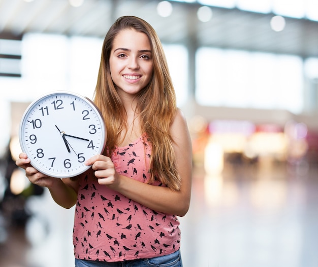 mujer joven sonriente y la celebración de un reloj en blanco