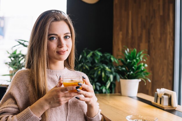 Mujer joven sonriente elegante que sostiene la taza de bebida en el contador de la barra en café