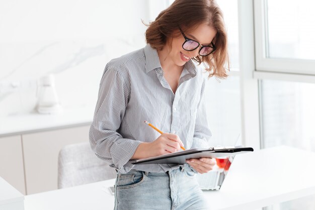 Mujer joven sonriente escribiendo en un portapapeles