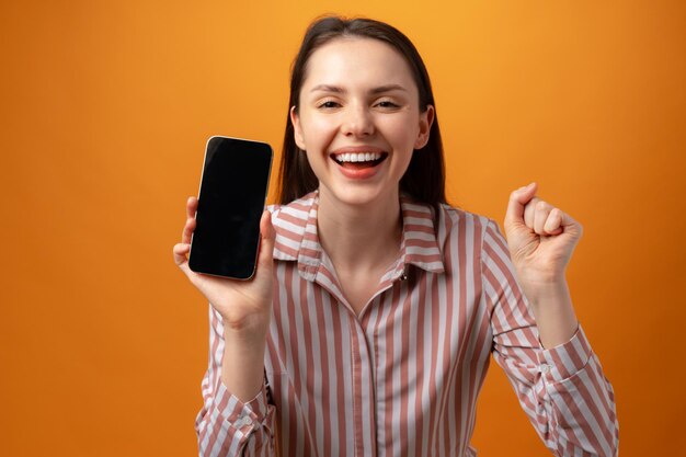 Mujer joven sonriente feliz que le muestra la pantalla negra del teléfono inteligente con espacio de copia