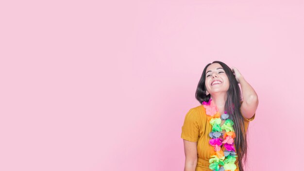 Mujer joven sonriente con la guirnalda falsa colorida que se opone a fondo rosado