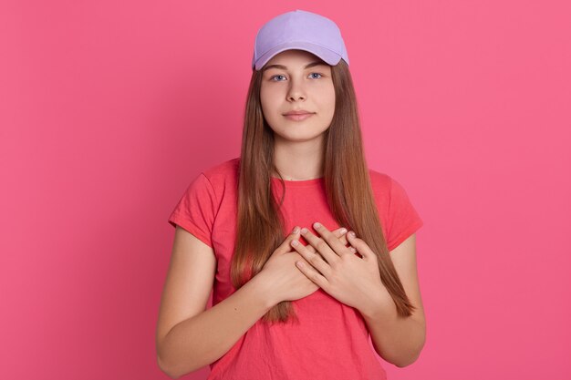 Mujer joven sonriente con las manos a su pecho aislado en la pared color de rosa