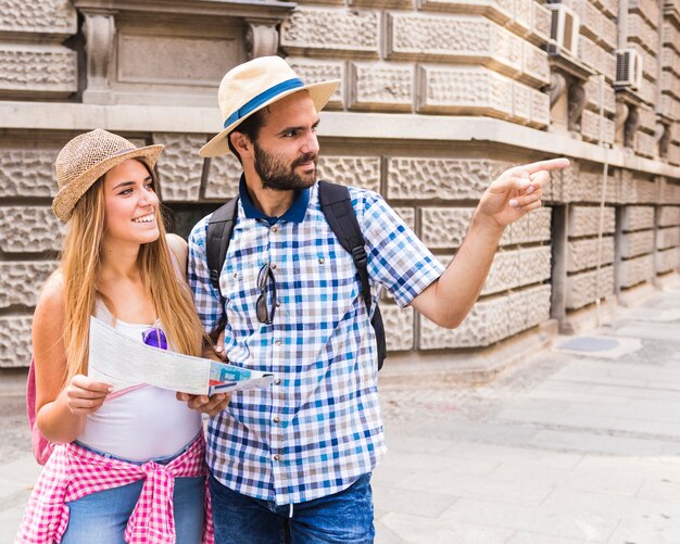 Mujer joven sonriente con el mapa que mira al hombre que muestra la dirección