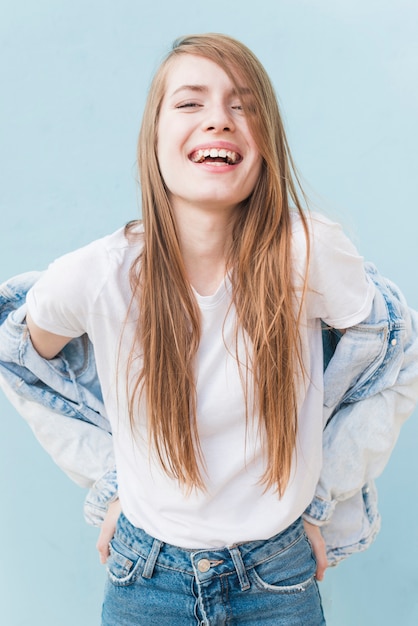 Mujer joven sonriente con el pelo rubio largo que se coloca en el contexto azul