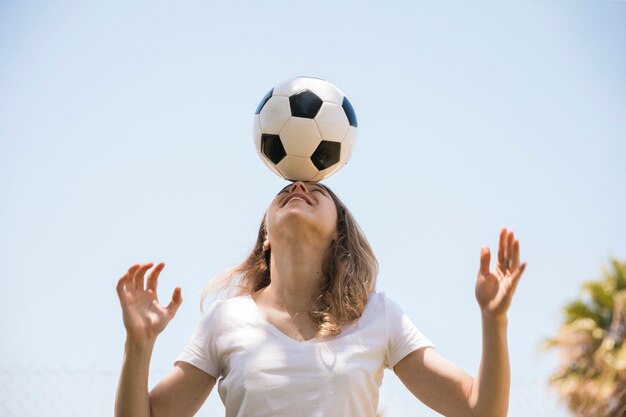 Mujer joven sonriente que balancea el balón de fútbol en la frente
