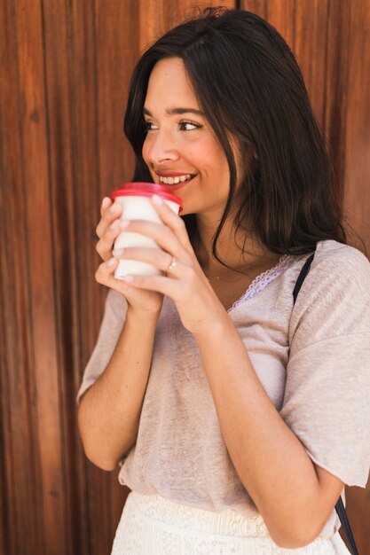 Mujer joven sonriente que bebe el café para llevar