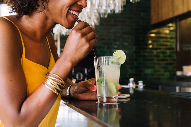 Mujer joven sonriente que bebe mojito en la barra del bar en el restaurante