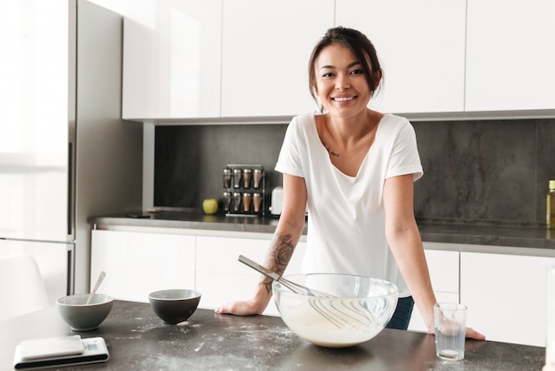 Foto gratuita mujer joven sonriente que se coloca en la cocina en casa