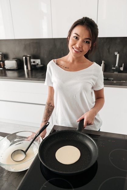 Mujer joven sonriente que se coloca en la cocina en casa