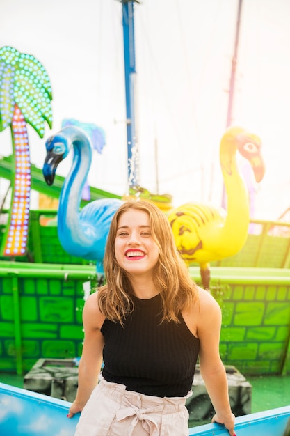 Mujer joven sonriente que se coloca delante de la fuente en el parque de atracciones