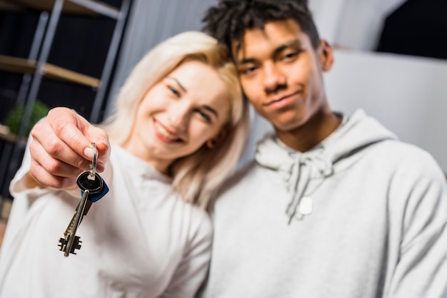 Mujer joven sonriente que se coloca con su novio que muestra llaves de la casa hacia cámara