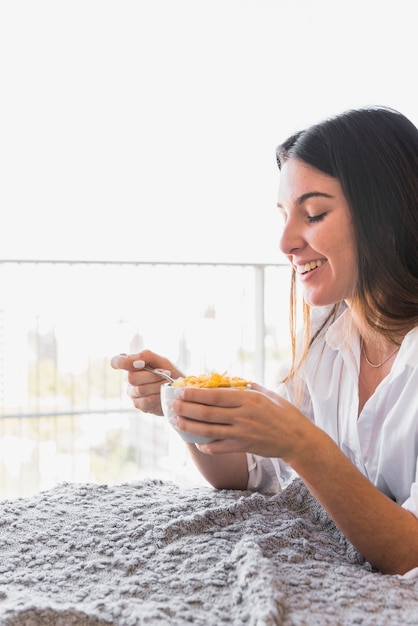 Mujer joven sonriente que disfruta del desayuno del copo de maíz