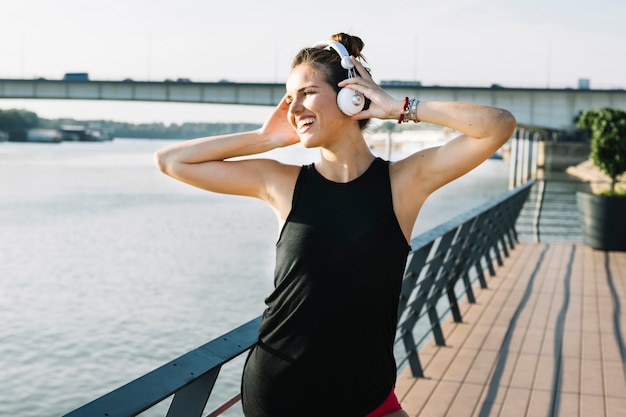 Foto gratuita mujer joven sonriente que escucha la música en el auricular cerca del río