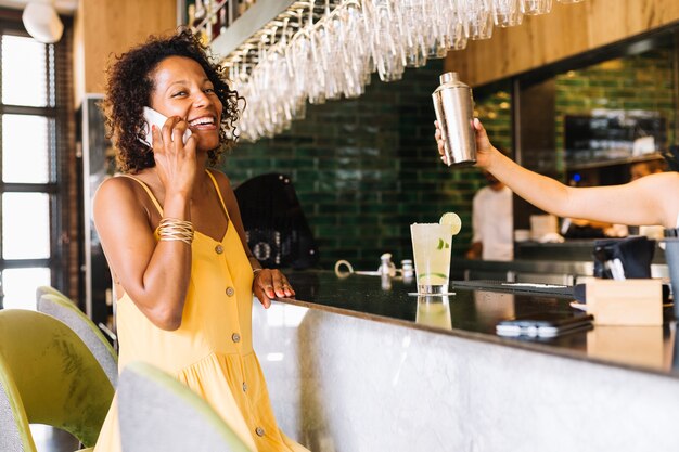 Mujer joven sonriente que habla en el teléfono móvil en el contador de la barra