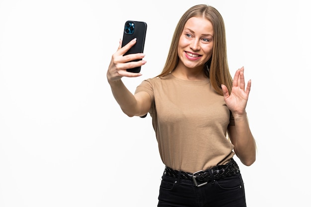 Mujer joven sonriente que hace la foto del selfie mientras agita la palma aislada en una superficie blanca