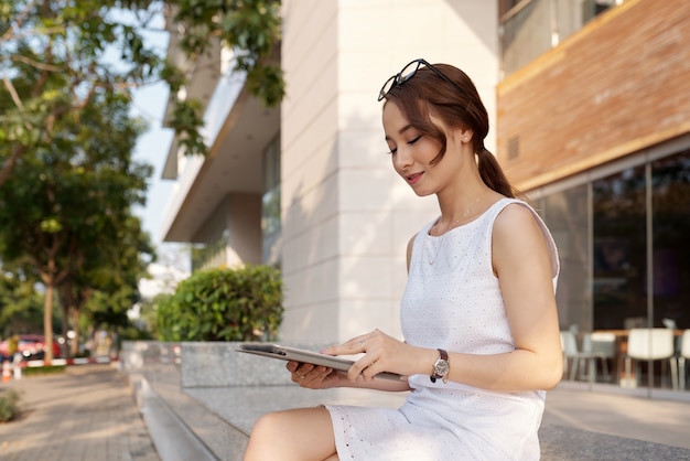 Mujer joven sonriente que lee datos en la tableta
