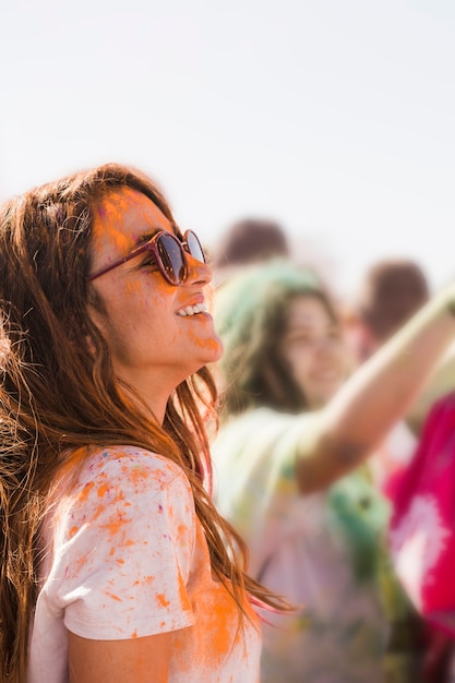 La mujer joven sonriente que lleva gafas de sol ensucia con un polvo anaranjado del holi