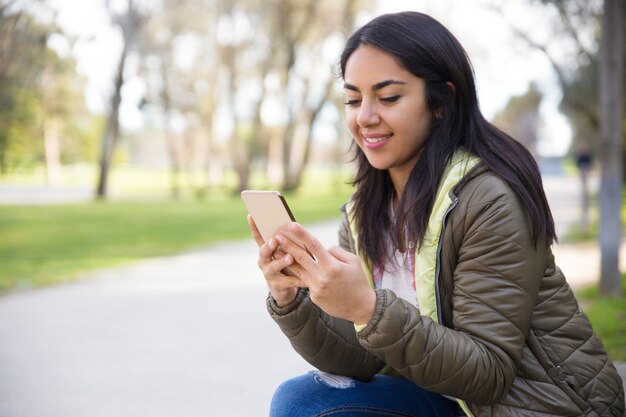 Mujer joven sonriente que manda un SMS al teléfono inteligente