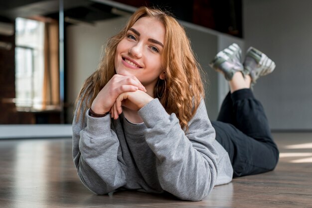 Mujer joven sonriente que miente en el piso que mira la cámara