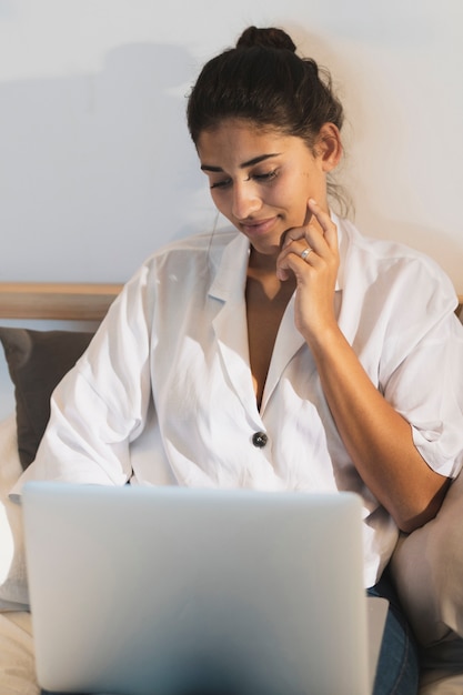 Mujer joven sonriente que mira en la computadora portátil