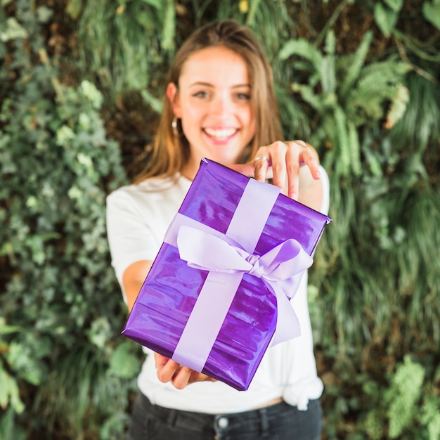 Mujer joven sonriente que muestra la caja de regalo púrpura