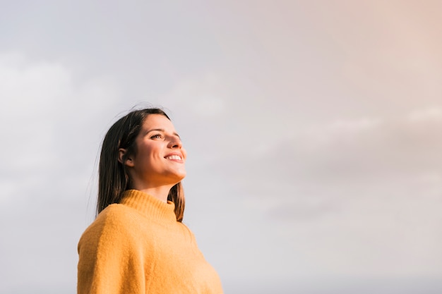 Mujer joven sonriente que se opone al cielo que mira lejos