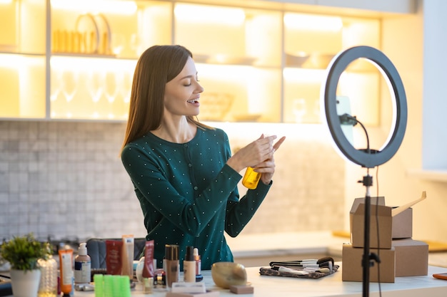 Mujer joven sonriente que presenta laca para el cabello durante el tutorial de belleza en línea