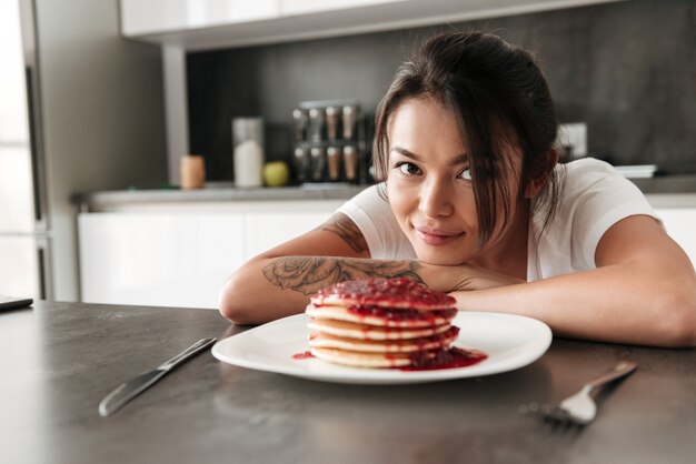 Mujer joven sonriente que se sienta en la cocina