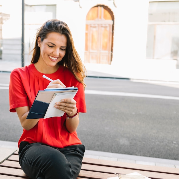 Mujer joven sonriente que se sienta en nota de la escritura del banco en diario