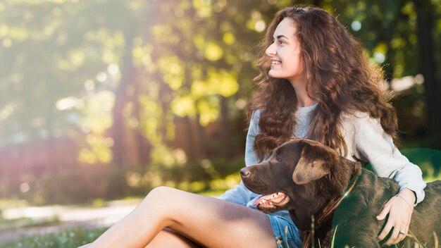 Mujer joven sonriente que se sienta con su perro en jardín