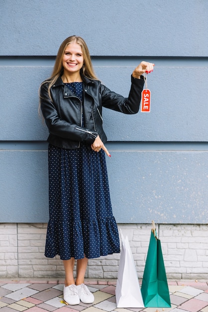 Foto gratuita mujer joven sonriente que sostiene la etiqueta de la venta en la mano que señala el dedo en los panieres