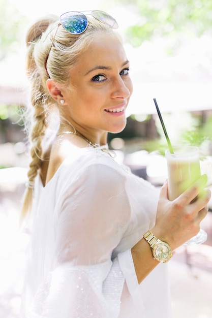 Mujer joven sonriente que sostiene el latte macchiato de cristal en la mano