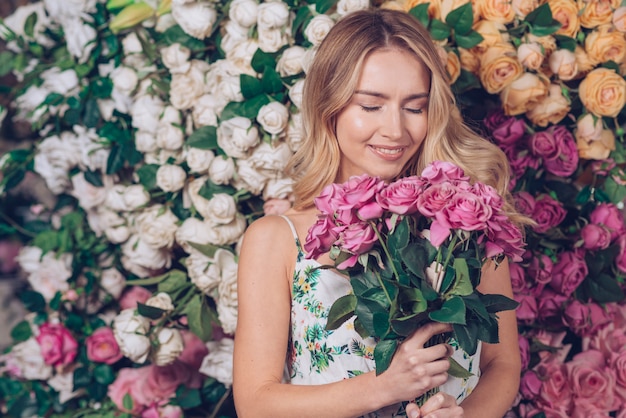 Foto gratuita mujer joven sonriente que sostiene rosas rosadas hermosas disponibles