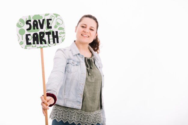 La mujer joven sonriente que sostiene salva la placa de la tierra contra el fondo blanco