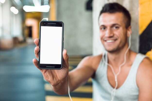 Mujer joven sonriente que sostiene el teléfono celular con la pantalla blanca en blanco