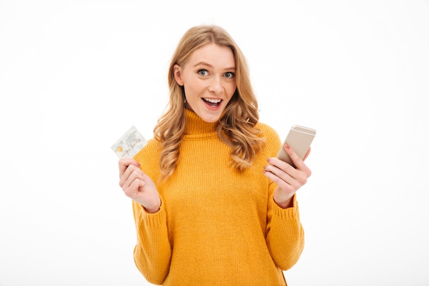 Mujer joven sonriente que sostiene el teléfono móvil y la tarjeta de crédito.