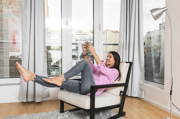 Mujer joven sonriente que toma el selfie en el teléfono móvil en casa