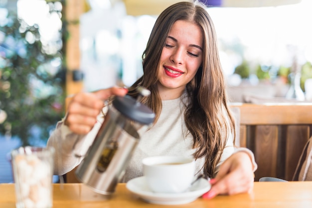 Mujer joven sonriente que vierte té de hierbas en la taza