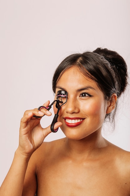 Mujer joven sonriente con rizador de pestañas