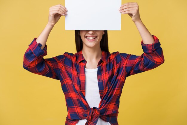 Mujer joven sonriente sosteniendo una hoja de papel blanco Retrato de estudio sobre fondo amarillo