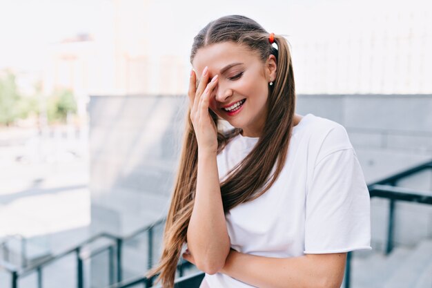 Mujer joven sonriente sosteniendo la mano en la cara y sonríe con los ojos cerrados