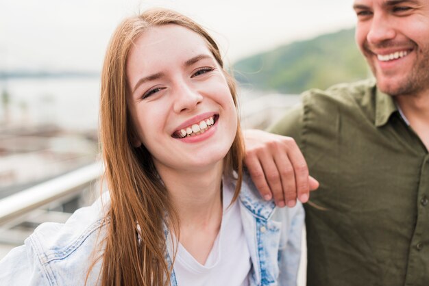 Mujer joven sonriente con su novio que mira la cámara
